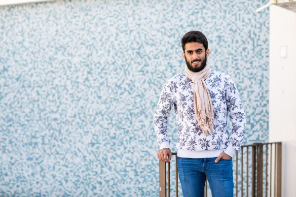 international male student wearing a wool scarf standing by a blue wall