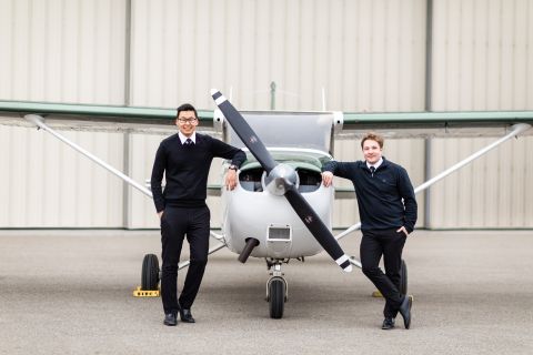 Two male commercial aviation students leaning on either side of a small propeller plane.