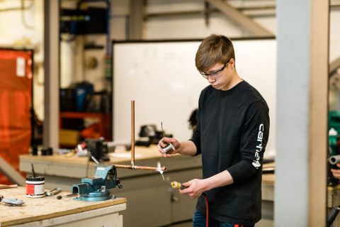 Apprentice heats up a piece of copper pipe with a torch