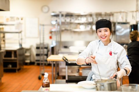Professional Cook apprentice ladles broth into a bowl