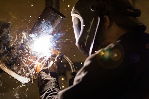Welding student watches closely as two metals are welded together amidst sparks