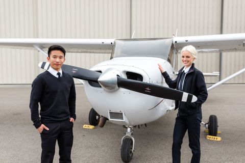 A male international student and a female student stand in front of a small airplane.