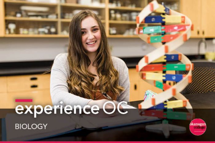 female student smiling with double helix model on table in front of her