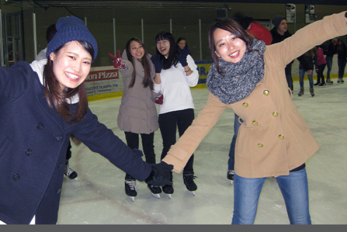Students holding hands, smiling and laughing while skating at an ice rink.