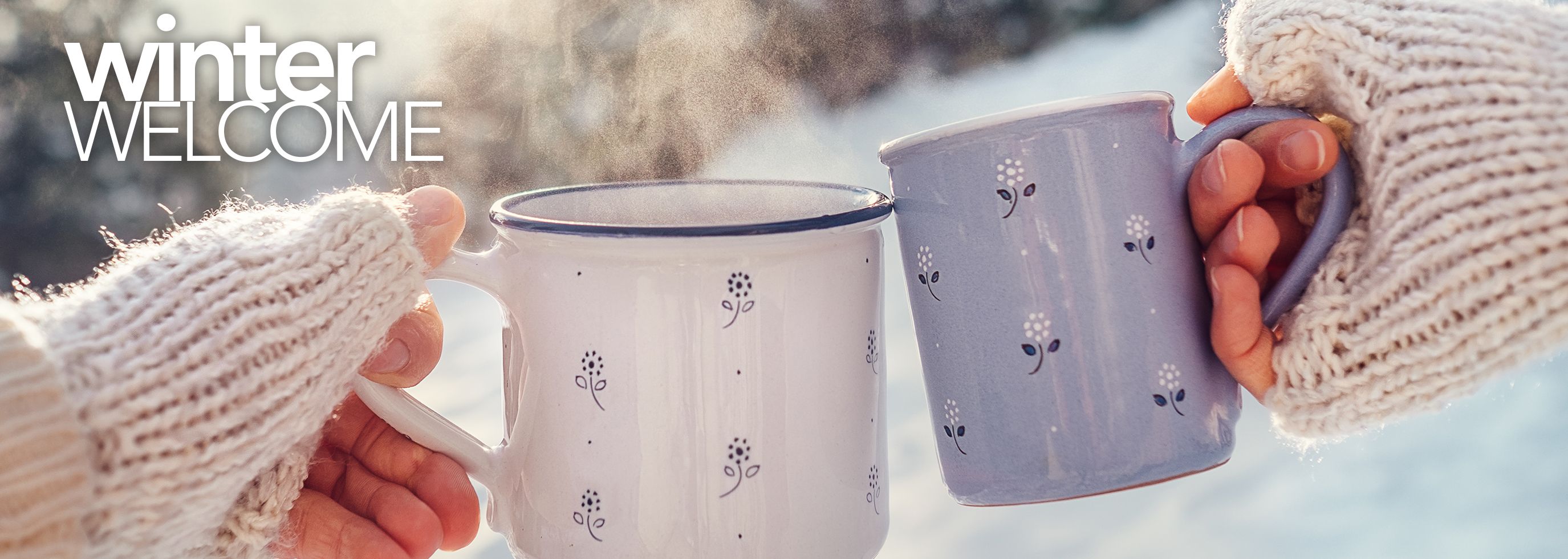 Winter scene with two hands each holding a mug with hot liquid