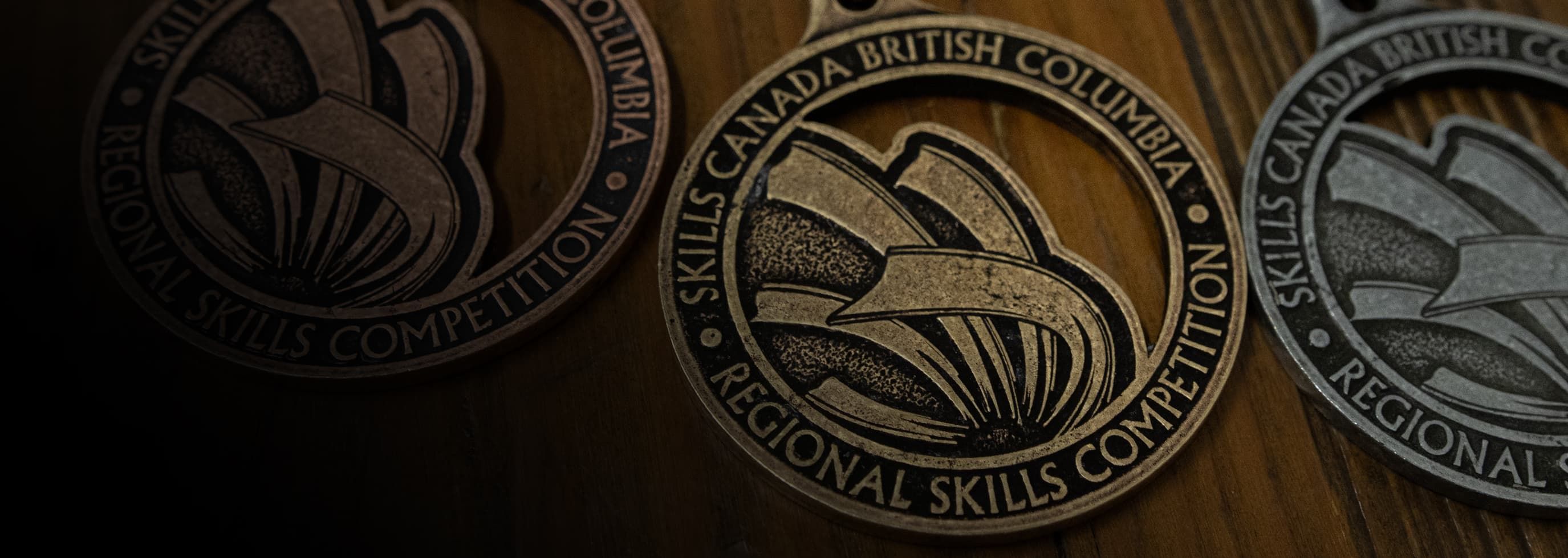 Three medals laying on the table, each bearing the words Skills Canada British Columbia Regional Skills Competition.