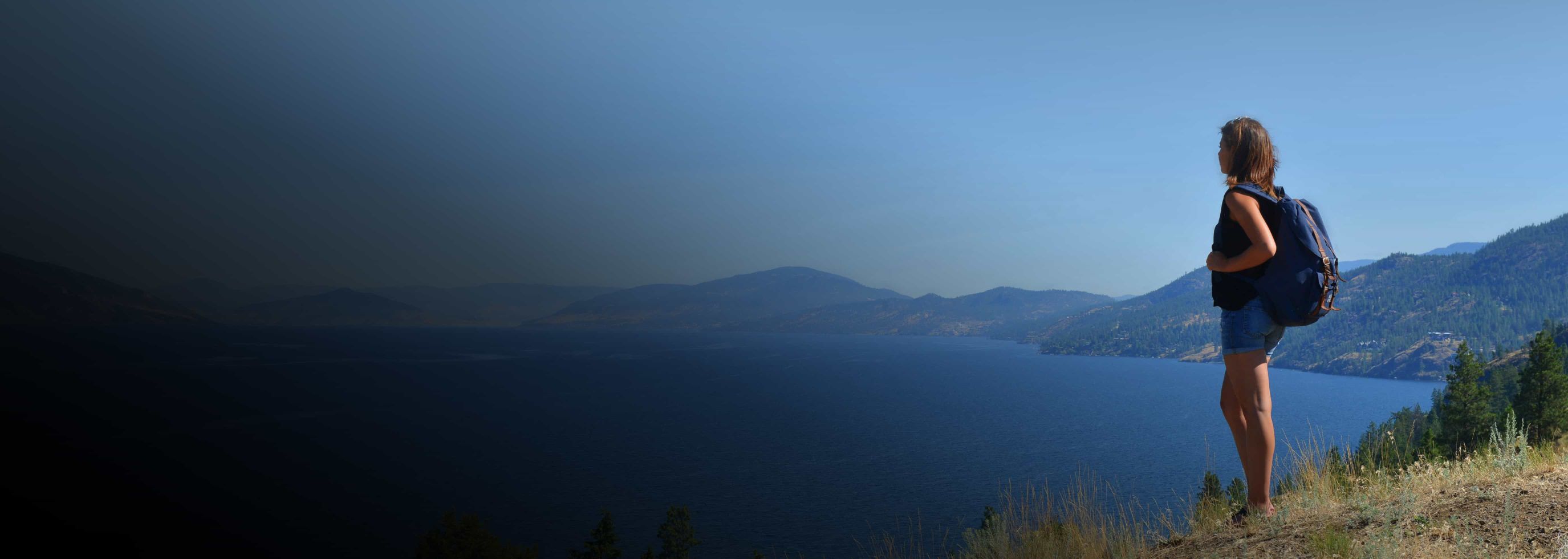 a person standing on a hill, gazing at a serene view of lake Okanagan