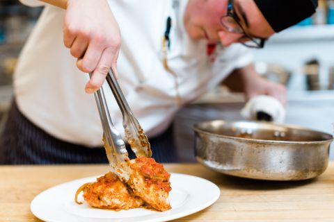 A male Culinary Arts student plates chicken from a saucepan. 
