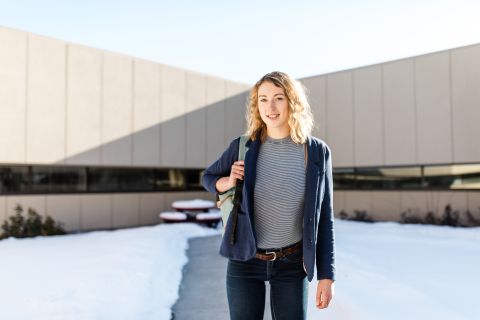 Female student stands outside holding a backpack in the winter.