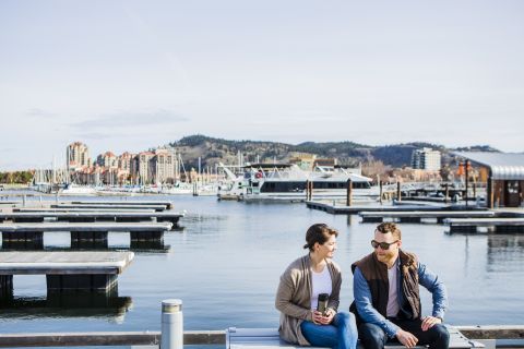 A female and male sitting on a bench having a conversation, drinking coffee in front of the waterfront.