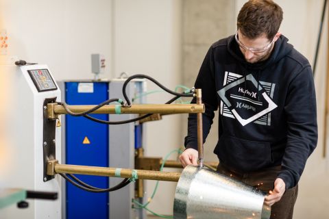 Sheet metal student uses machinery to bind two metals together in a cone shape