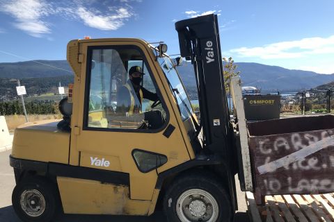 student driving a yellow forklift lifting a wooden pallet with beautiful clear sunny sky in the background