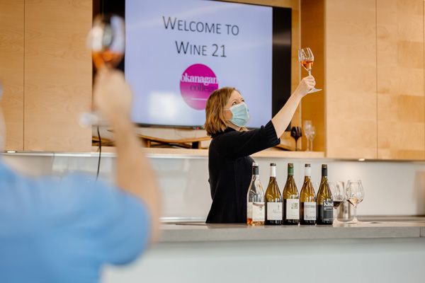 Mireille at the front of a classroom holding a glass of wine while wearing a face mask
