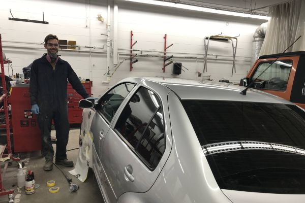 Collision Repair student, Karl, stands in front of a silver car that he repaired