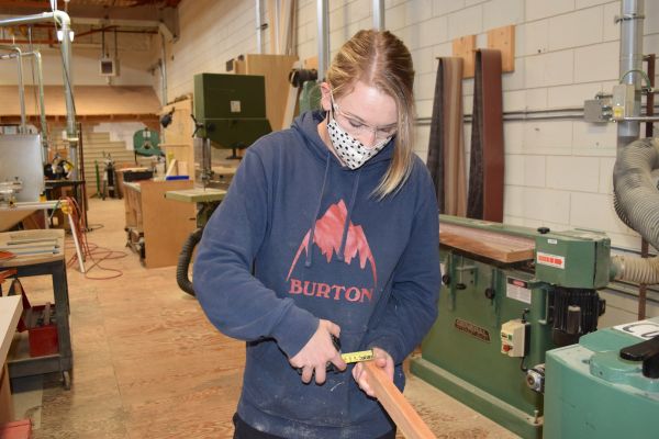 Female carpentry student measures a piece of wood with a tape measure