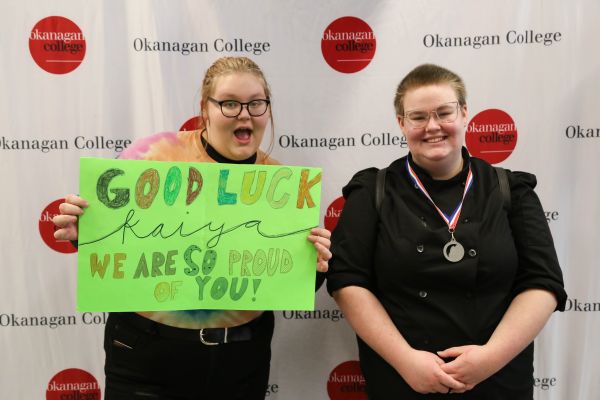 Culinary Arts Skills Regional medalists stands next to her supporter who is holding a celebration sign