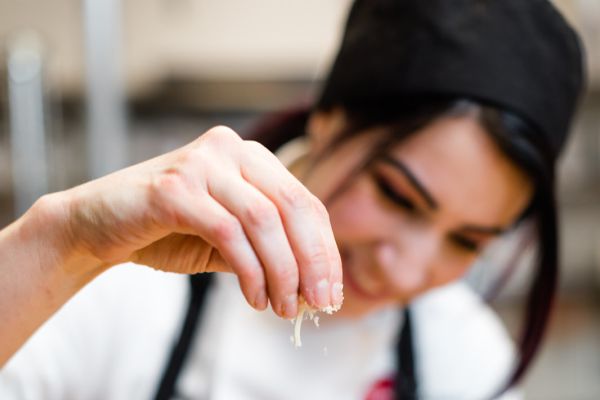 culinary arts student with apron and cooking cap sprinkling product onto table surface