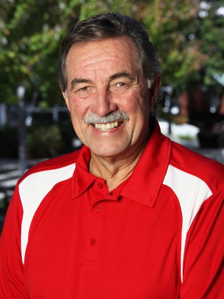 Headshot of Dennis Gabelhouse wearing a red shirt with green trees behind him