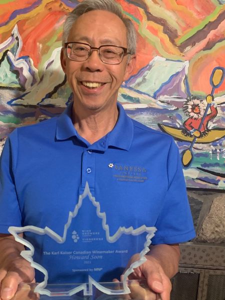 Howard Soon wearing a blue shirt holding a glass award in the shape of a maple leaf