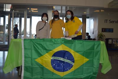 Three women pose together in front of Brazil's national flag during International Education Week at Okanagan College's Kelowna campus