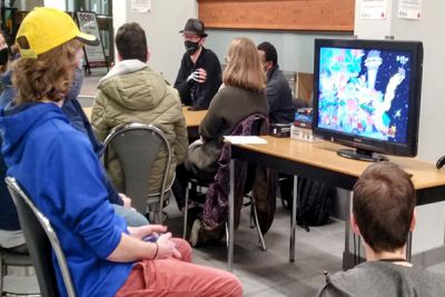 Students are playing video games while other students talk to each other in the background.