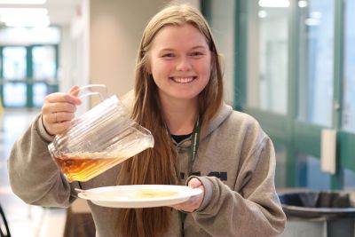 Student pours maple syrup on pancakes during Giving Tuesday fundraiser