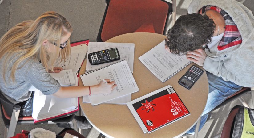 One male and one female student sitting at a round table with notebooks and calculators
