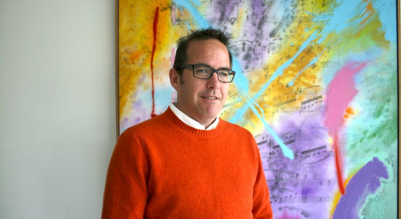 Psychology Professor Chris Newitt stands in front of a colourful painting