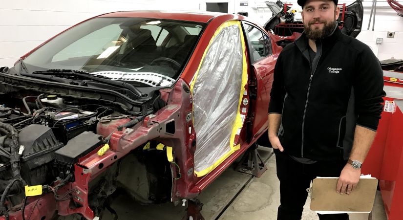 Collision Repair instructor Andreas Roth stands beside a disassembled vehicle being prepped for repair.