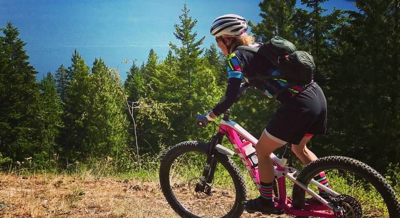 Kinesiology Professor Louise Blais rides her mountain bike on a hill with trees overlooking Okanagan Lake