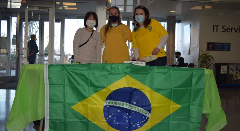 Three women pose together in front of Brazil's national flag during International Education Week at Okanagan College's Kelowna campus