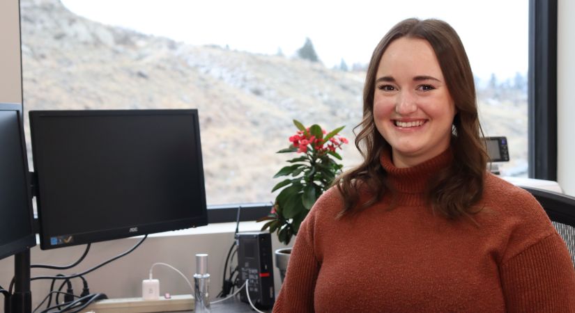 Electronics engineering alum Emily Schatz sits at a computer desk by a window overlooking the mountain