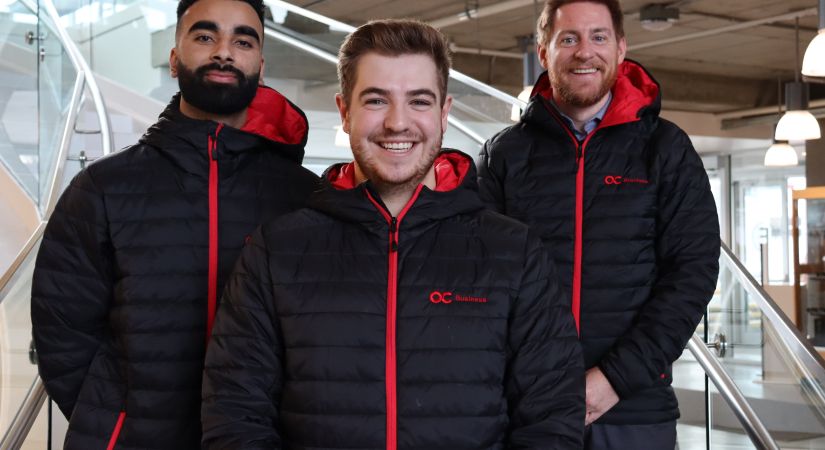 Three OC Finance team, business competitors, stand smiling wearing black and red Okanagan College jackets